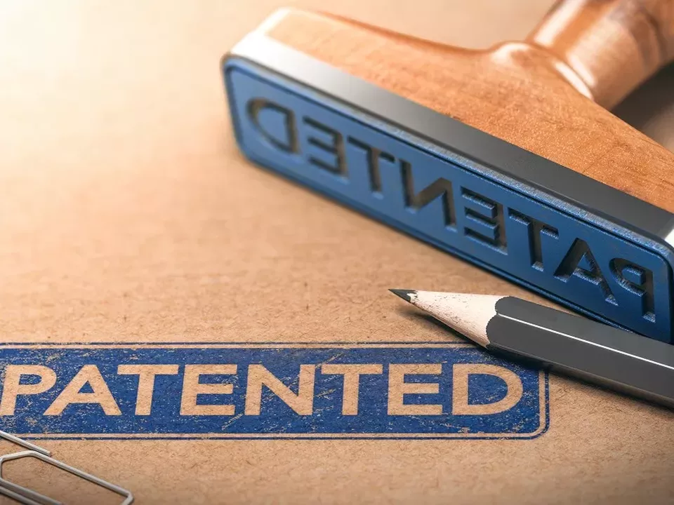 FlexQube får patent i USA Brunt papper med en blå stämpel där det står "patented" och själva stämpeldynan ligger bredvid tillsammans med en grå blyertspenna.